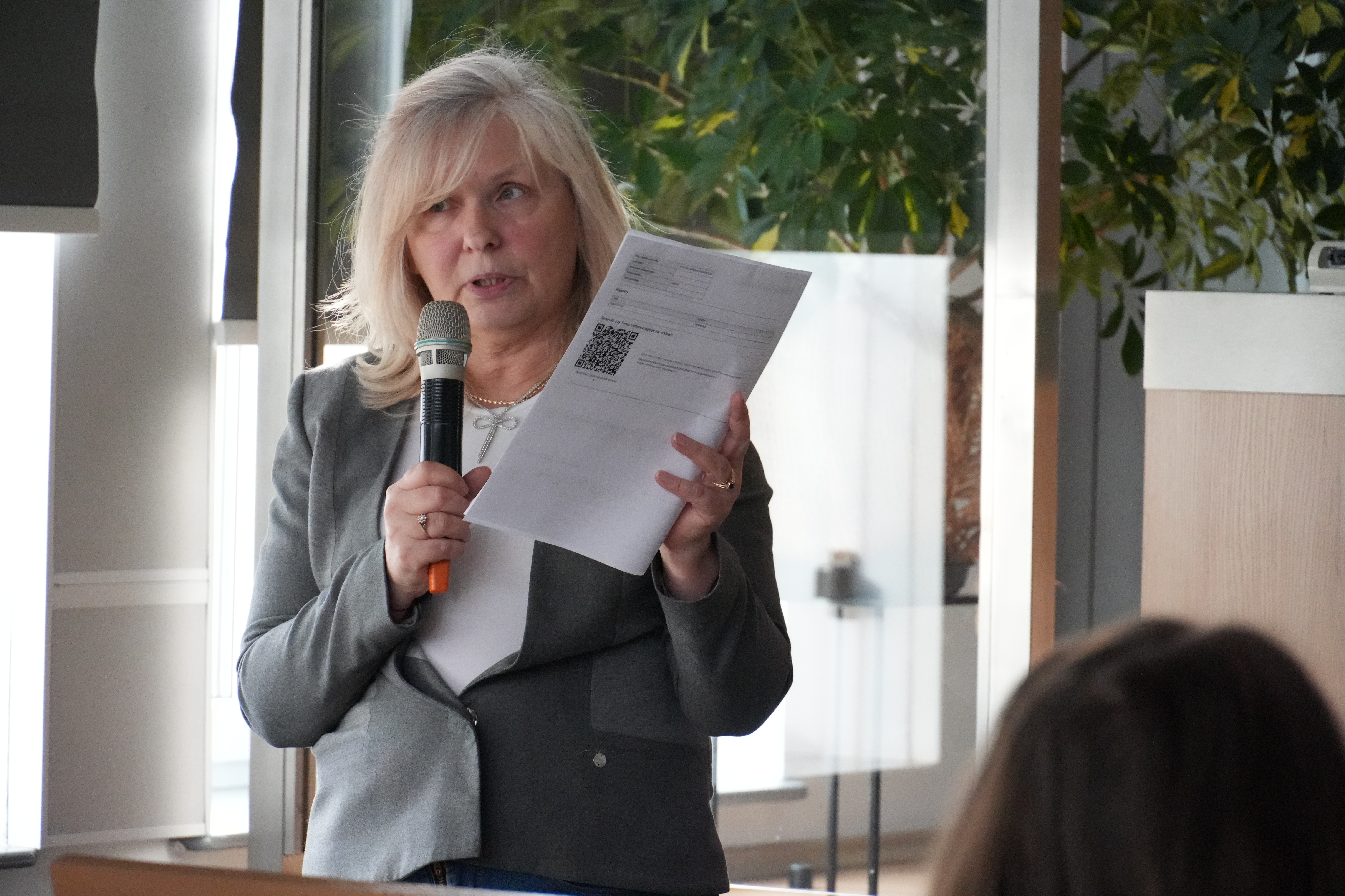 Zdjęcie kobiety trzymającej mikrofon i kartkę, która prowadzi szkolenie.