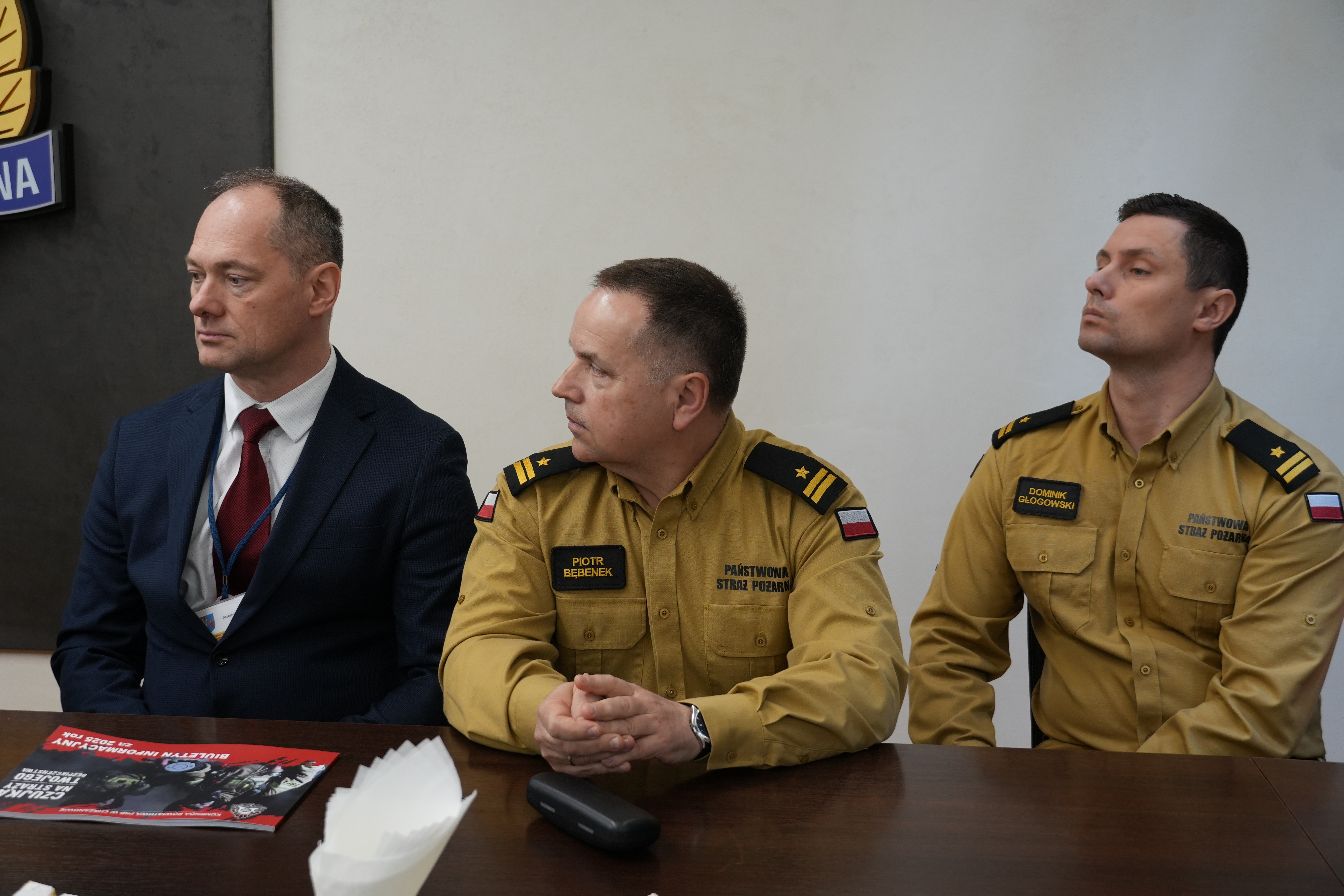 Trzech mężczyzn,w tym dwóch w mundurach strażackich, jeden w garniturze 