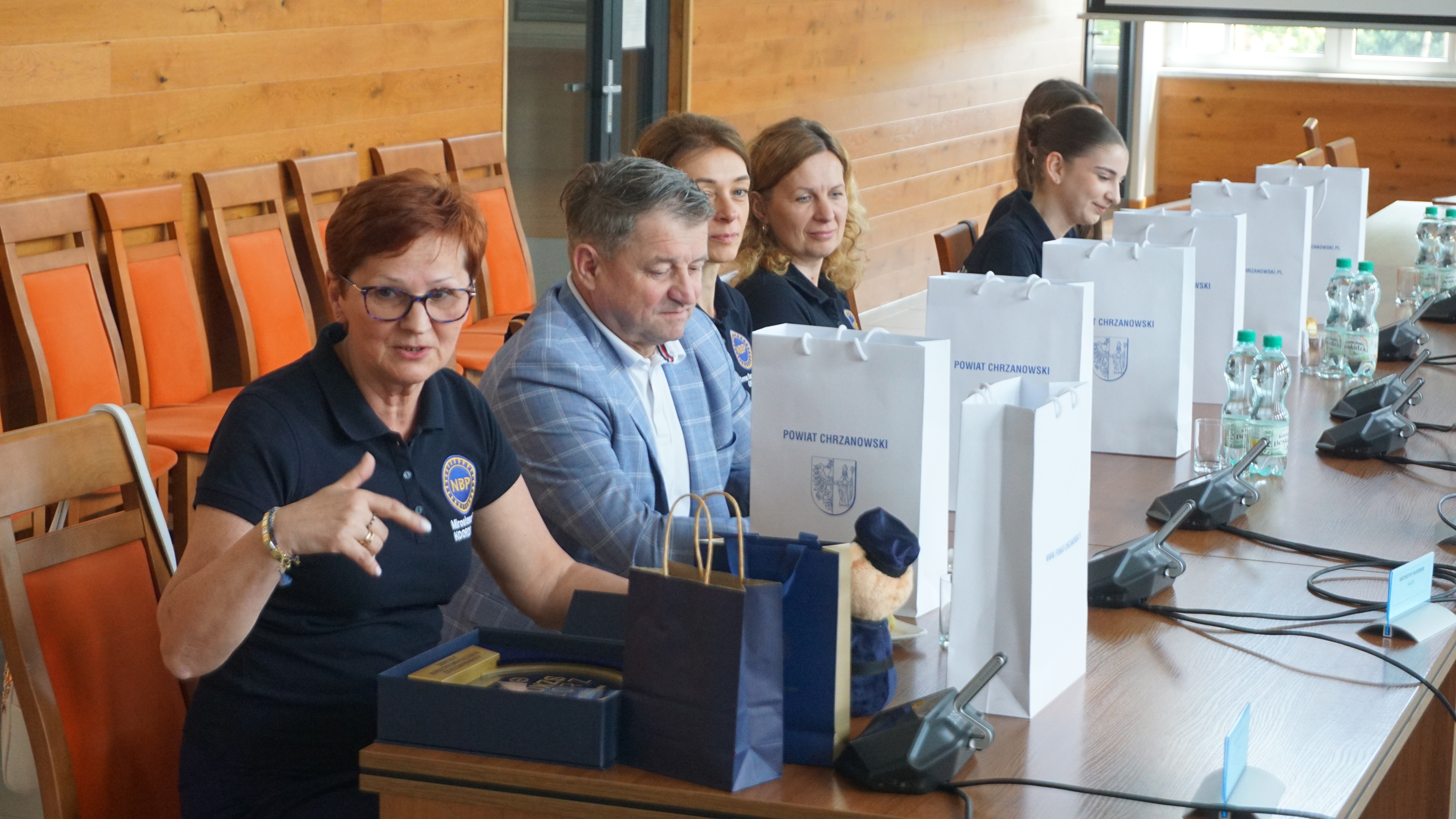 Zdjęcie pięciu osób, opiekunów i uczniów siedzących przy stole. Jeden z opiekunów mówi i gestykuluje.