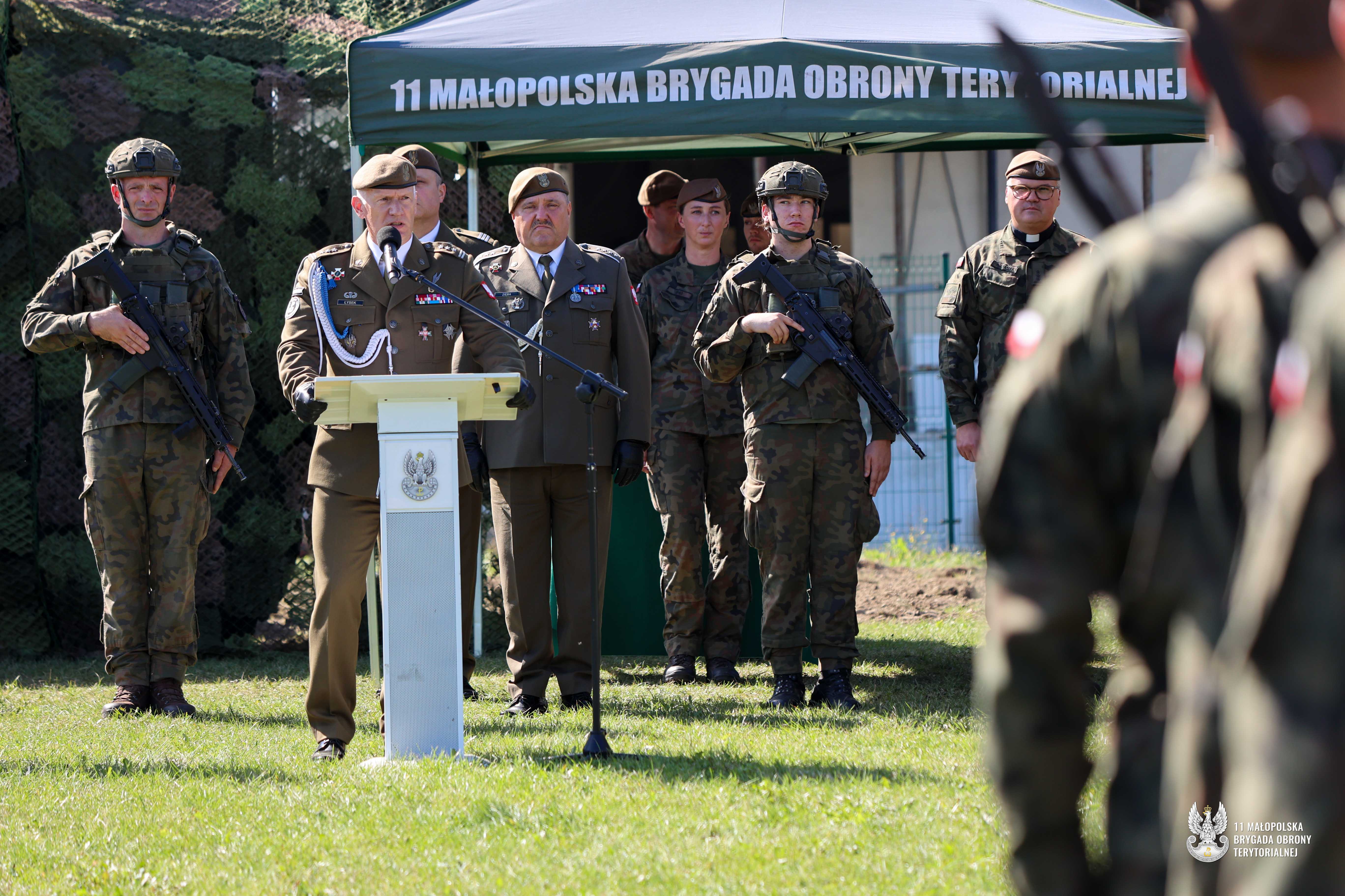 Kilkanaście żołnieży podczas uroczystości. Jeden z dowódców stoi za mównicą.