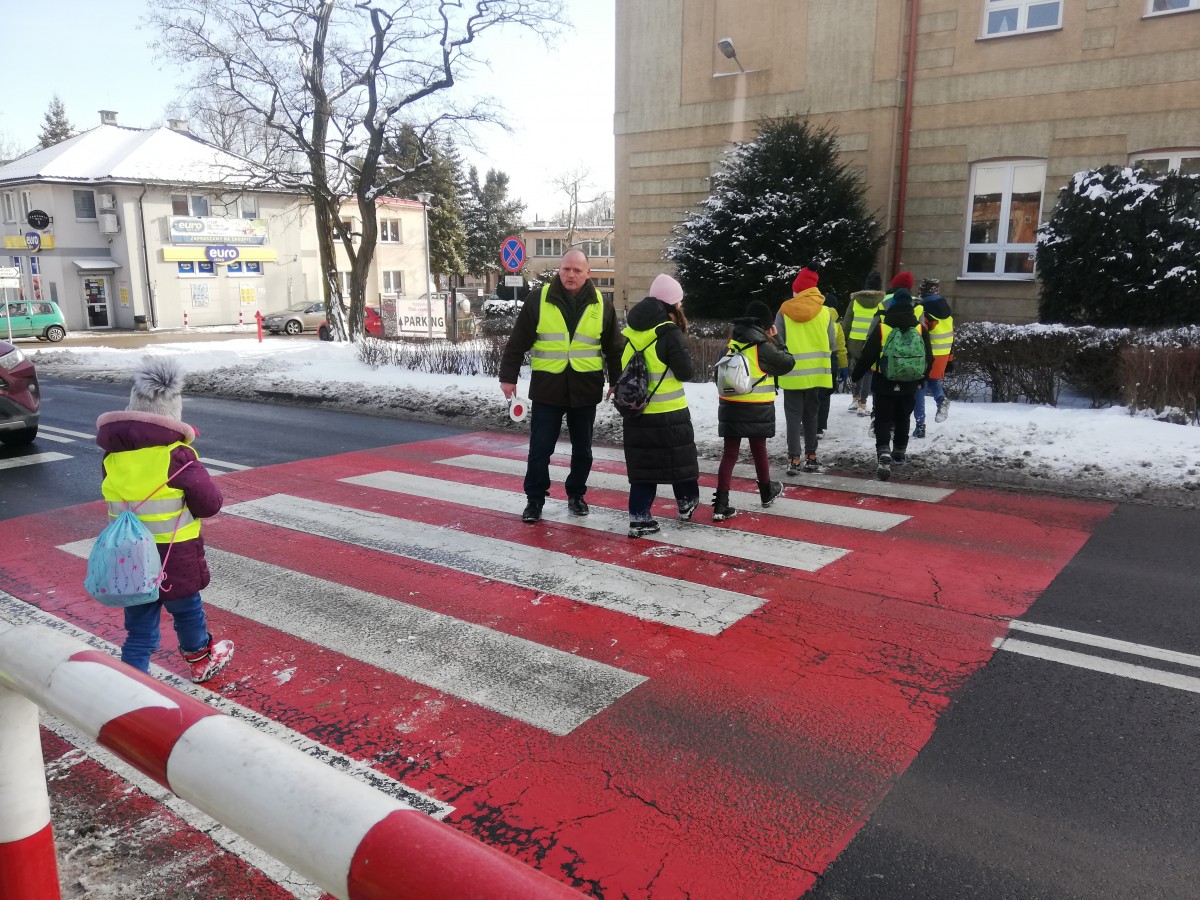 Dzieci w kamizelkach odblaskowych przechodzą przez przejście dla pieszych 