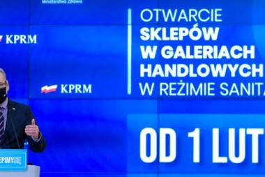 banner po lewej stronie minister zdrowia w maseczce, po prawej napis od 1 lutego otwarcie sklepów w galeriach handlowych w reżimie sanitarnym tło niebieskie w tle flagi polski i napis KPRM 