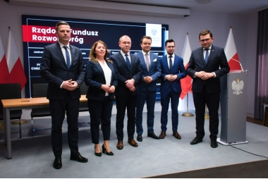 Pięciu mężczyzn i jedna kobieta stoją obok siebie, w garniturach. Uśmiechają się 