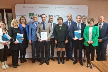 zdjecie grupowe przedstawiciele gmin, powiatu oraz firmy doeko  12 osób stoi i prezentuje podpisane porozumienie w tle ścianka promujaca gminę babice 