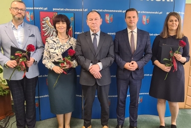 Trzech mężczyzn i dwie kobiety stoją na tle niebieskiej ścianki z białymi napisami i herbem w kolorze czerwono, żółto niebiesko białym w czarnej ramce