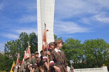 Przebrani za powstańców warszawskich młodzi ludzie stoją na baczność przy pomniku 