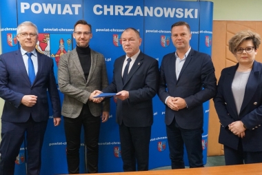 Czterech mężczyzn i jedna kobieta stoją przy tablicy Powiat Chrzanowski 