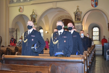 Mężczyźni  w mundurach strażackich stoją w ławach kościelnych