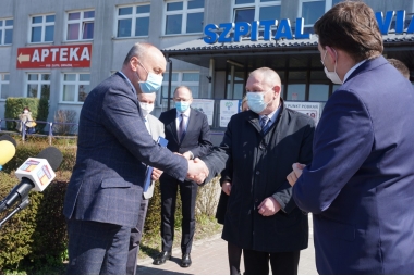 Mężczyźni stoją przed budynkiem szpitala i podają sobie ręce 