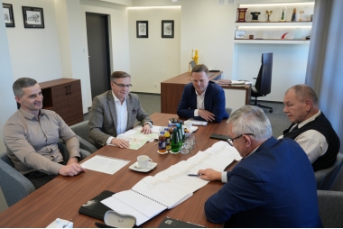 Zdjęcie pięciu mężcyzzn siedzacych przy stole. Przed nimi znajduje się kilka dokumentów. 