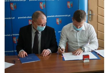 Mężczyźni podpisują umowę na tle ścianki z napisem Powiat Chrzanowski 