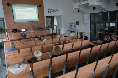 Zdjęcie sali wykładowej z kilkudziesięcioma osobami. Jedna osoba stoi przy na środku sali i prowadzi szkolenie, reszta osób siedzi.