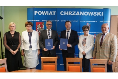 dyr ops, skarbnik libiaża, wiceburmistrz Libiąża, wicestarosta, skarbnik powiatu, cżł. zarządu powiatu stoja przed niebieską ścianką z herbami powiatu chrzanowskiego. WST i Wiceburmistrz prezentują teczki z podpisaną umową 