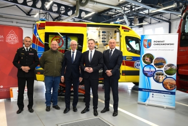 Pięciu mężczyzn pozuje do zdjęcia. W tle karetka, banery promocyjne