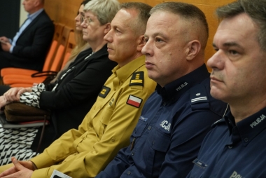 Dwóch policjantów, strażak, dwie kobiety. Wszyscy w pozycji siedzącej 