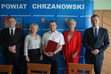 Dwie kobiety i trzech meżczyzn na tle niebieskiego baneru z herbem  powiatu chrzanowskiego 