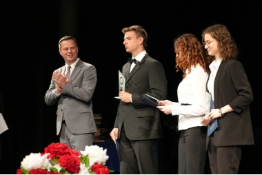 Zdjęcie czterech osób. Mężczyzny i trójki uczniów. Mężczyzna klaszcze spoglądając na stojących obok uczniów, którzy trzymają dyplomy i statuetki.
