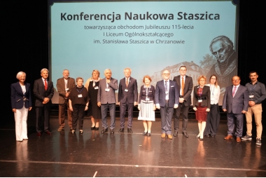Zdjęcie kilkunastu osób na scenie. W tle rzutnik wyświetlający plansze związaną z wydarzeniem.