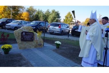 Ksiądz w szatach liturgicznych kropi kropidłem kamień 