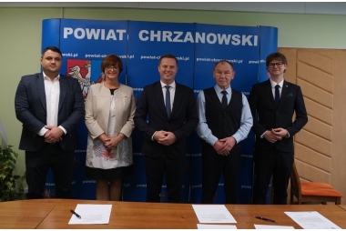 zdjęcie portretowe , członkowie zarządu powiatu chrzanowskiego stojją obok siebie , w tle scianka niebieska z herbami powiatu 