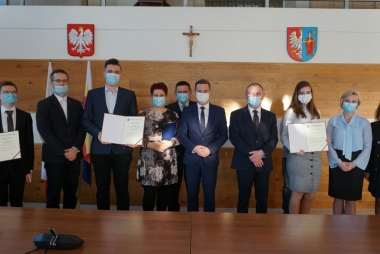 Dziesięcioosobowa grupa pozuje do zdjęcia. W grupie są osoby w różnych wieku, wszyscy w maseczkach. 