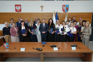 Zdjęcie kilkundziesięciu osób. Niektóre osoby trzymają w rękach teczki i róże.