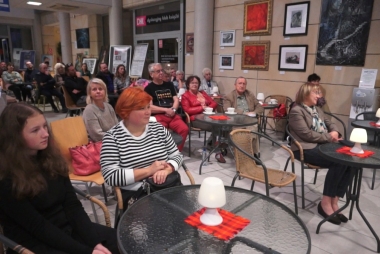 Osoby w różnym wieku siedzą przy stolikach. Na blatach lampki 