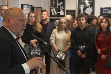 Do mikrofonu przemawia mężczyzna, w tle inne osoby