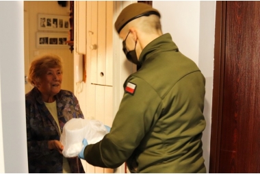 na zdjeciu żołnierz wręczajacy seniorce zakupy
