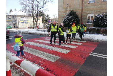 Dzieci w kamizelkach odblaskowych przechodzą przez przejście dla pieszych 