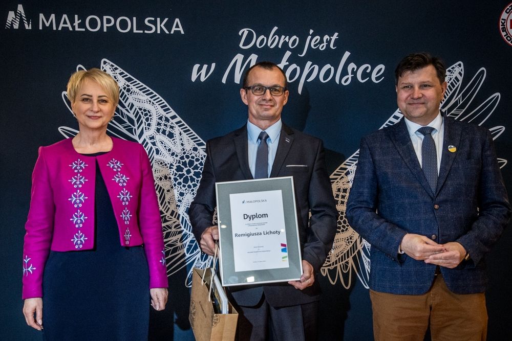 Kobieta w różowej marynarce i dwóch mężczyzn, jeden z dyplomem w rękach 